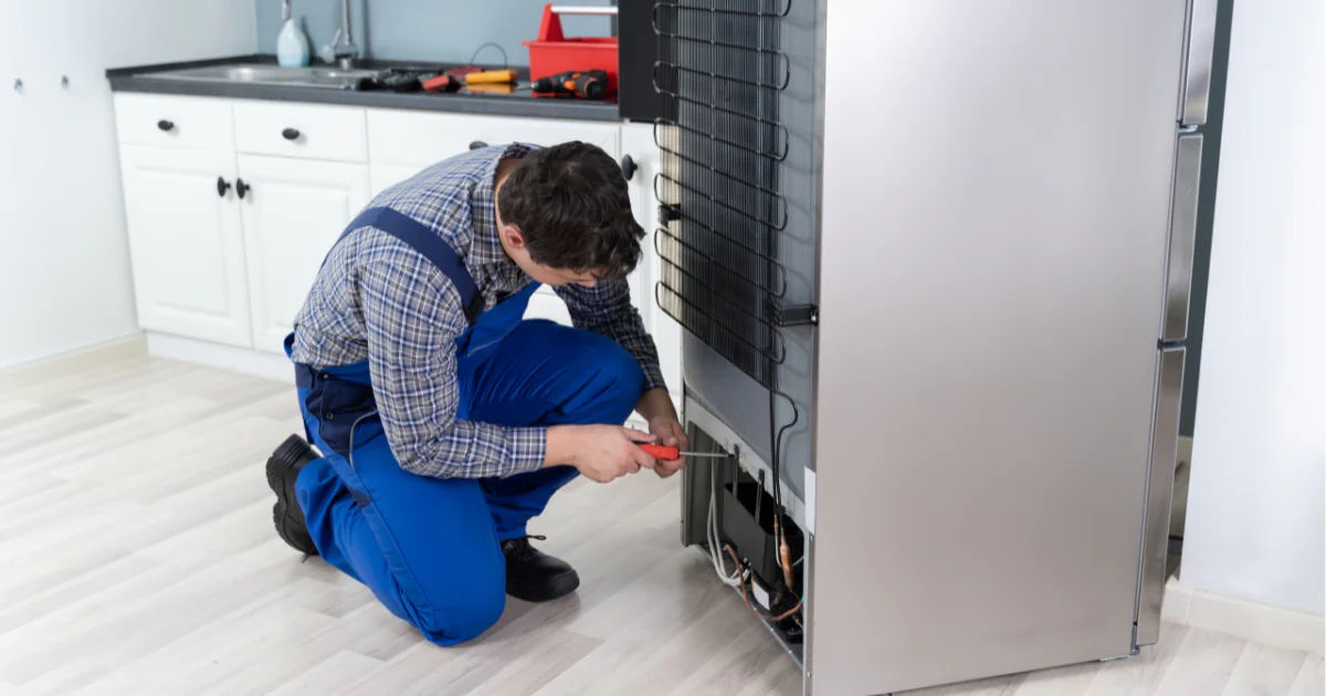 A person in overalls fixing a refrigerator