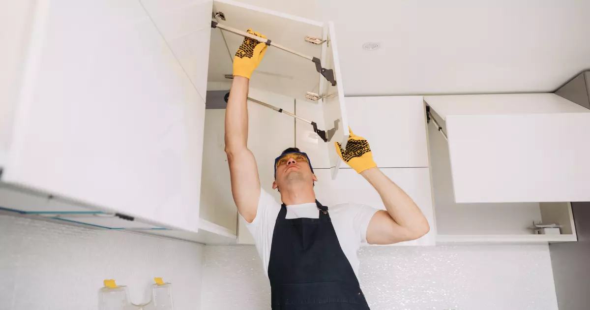 A person in a black apron and yellow gloves fixing a white cabinet